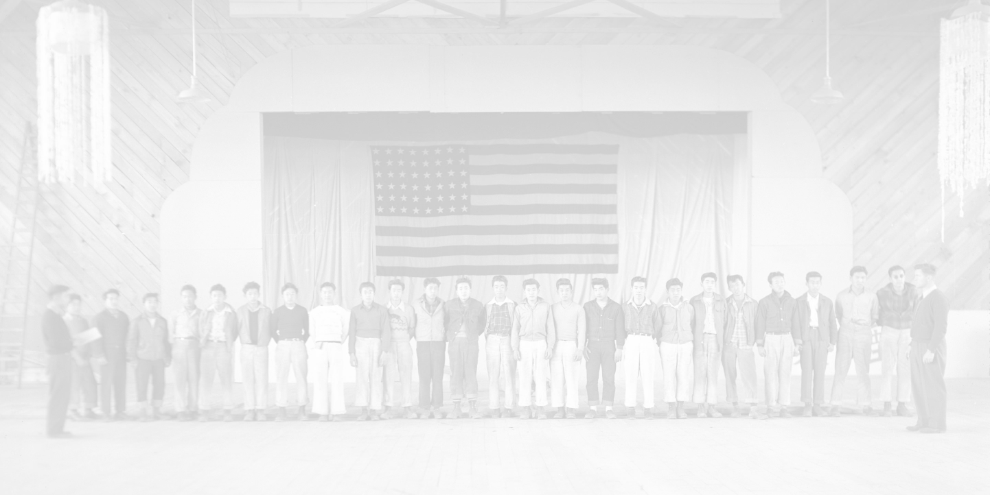 A group of Japanese americans lined shoulder to shoulder in a ballroom with a large american flag hung behind them